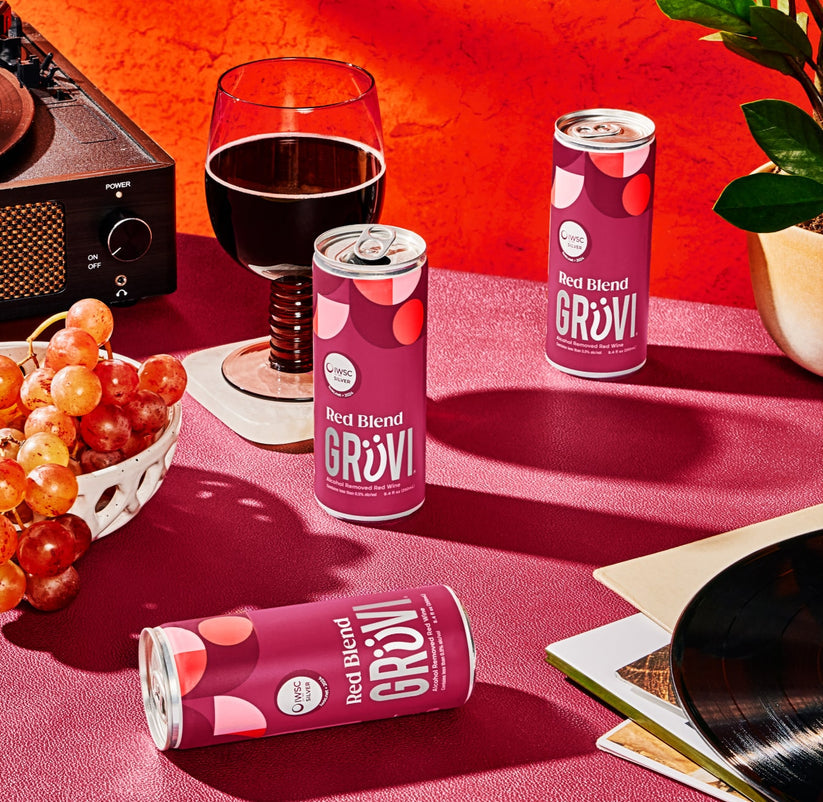 Gruvi Red Blend cans on a table with a glass of wine and grapes on the side