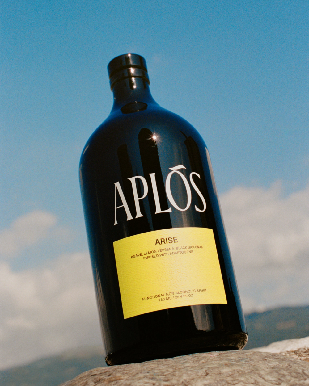 Black bottle of Aplos Arise gin with a yellow label against a blue sky.