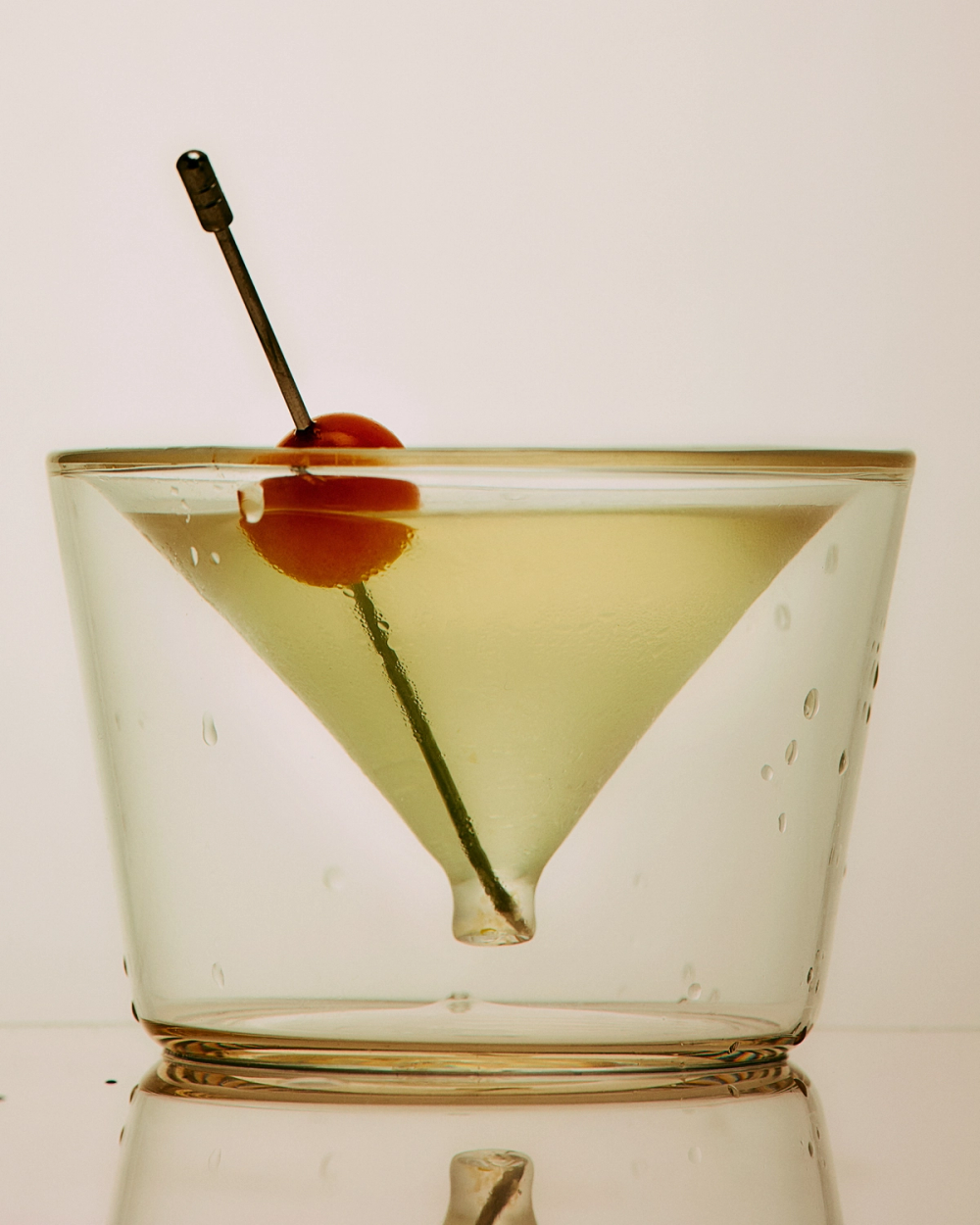 Cocktail in a martini glass with a cherry and olive on a white background