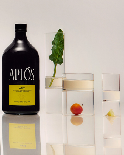 Black bottle labeled 'Aplós' with a glass containing a leaf and peach on a light background