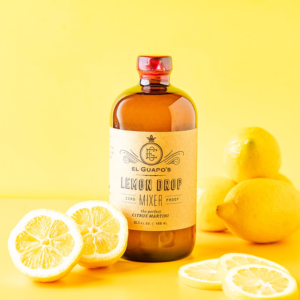 Bottle of El Guapo's Lemon Drop Mixer with lemons on a yellow background