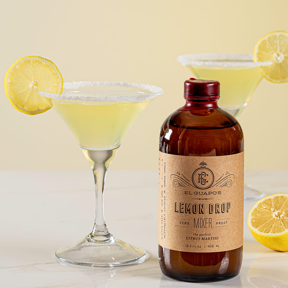 Bottle of lemon drop mixer with a cocktail and lemons on a light background