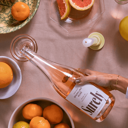 Surely Sparkling Rose being served at birds eye view over a dining table with citrus fruits on it.
