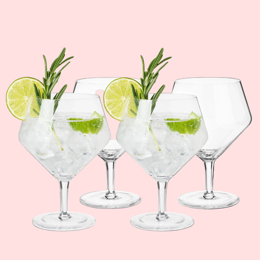 Set of four gin glasses with lime and rosemary garnishes on a white background